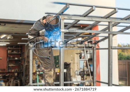 Metalworker performs welding on a structure in a residential backyard surrounded by nature in autumn afternoon light