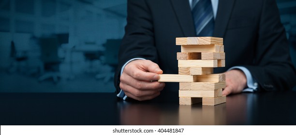 Metaphor of risk in business. Risk management concept. Businessman remove one piece from tower, wide banner composition with office in background. Nothing ventured, nothing gained.