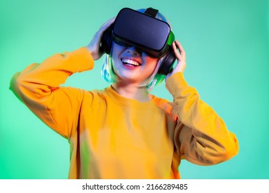 Metaverse concept, close up young asian woman in yellow sweatshirt wearing vr headset playing watching on the green screen background.
