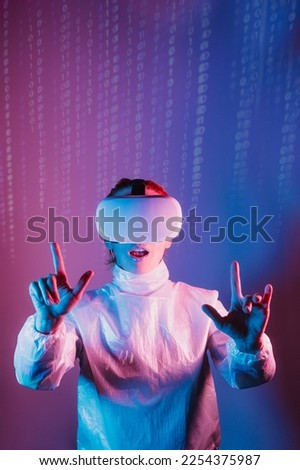 Metaverse concept. Woman in holographic clothes and vr glasses on matrix code background. Person with virtual reality headset, trying to touch something with hand in pink blue colors. Vertical card.