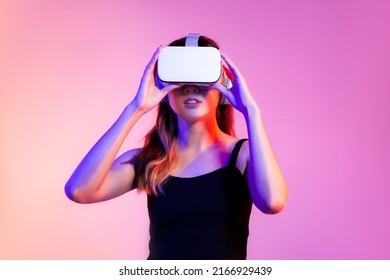Metaverse concept young asian woman in black tank top wearing white vr headset watching 3d online on pink screen background.
