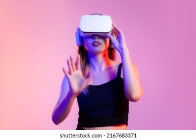 Metaverse concept, young asian woman in black tank top wearing white vr headset watching playing and touching on pink neon color background.