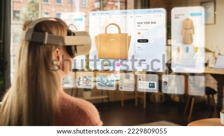 Metaverse Futuristic Concept: Woman Using Virtual Reality Headset to Shop Online from Home while Sitting in Stylish Cozy Living Room. Over the Shoulder Footage of a Female Shopper Choosing a Bag