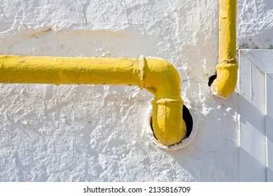 Methane Gas And Water Yellow Metal Pipe Against A White Rough Plaster Wall 