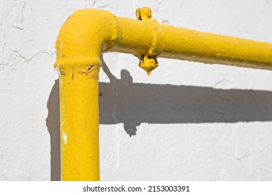 Methane Gas And Water Yellow Metal Pipe Against A White Rough Plaster Wall 