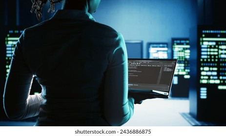 Meticulous expert working in server hub, running code on laptop, monitoring technologically advanced electronics clusters of blade servers, networking systems and storage arrays