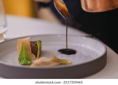 Meticulously plated gourmet dish with meat, green leaves, and crispy elements, finished with dark sauce from a copper pot. High-end dining in a luxury hotel. - Powered by Shutterstock