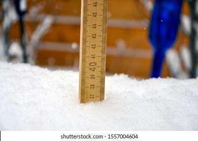 A Metre Stick Registers A Huge Snowfall In The Garden. A Decorative Blue Glass Bottle Can Be Seen In The Background.