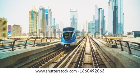 Metro train on Red line in Dubai downtown with skyscrapers at background.