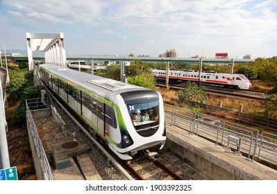 A metro train of Taichung MRT traveling thru a bridge near the High Speed Rail Station and a Puyuma Express train passing-by on the railway in the background, in Wuri District, Taichung City, Taiwan