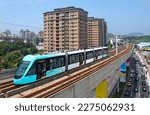 A metro tram traveling on the elevated track of Danhai Light Rail Transit on a beautiful sunny day, with booming residential towers in the nearby community, in Tamsui District, New Taipei City, Taiwan