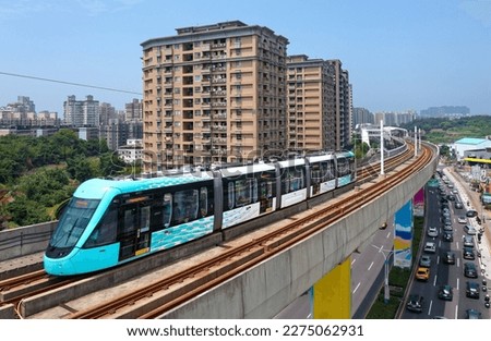 A metro tram traveling on the elevated track of Danhai Light Rail Transit on a beautiful sunny day, with booming residential towers in the nearby community, in Tamsui District, New Taipei City, Taiwan