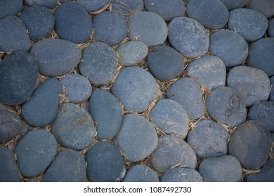 Mexican Beach Pebbles Cover A Small Flat Area Of Ground, Straw Or Dead Grass Between Stones. Garden Ground Cover.