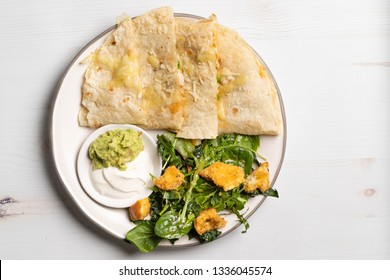 Mexican Cheese Chicken Quesadilla Served With Fresh Guacamole And Sour Cream On An A Mini Plate. Served With A Side Kale And Super Green Salad With Homemade Croutons. Table Top View 