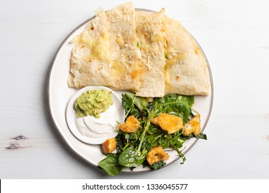 Mexican Cheese Chicken Quesadilla Served With Fresh Guacamole And Sour Cream On An A Mini Plate. Served With A Side Kale And Super Green Salad With Homemade Croutons. Table Top View 