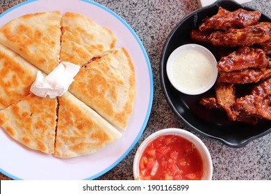 Mexican Chicken Quesadillas With Cheese On White Plate And Bbq Chicken Wings On Dark Plate With Sauce, Top View. Mexican Food.