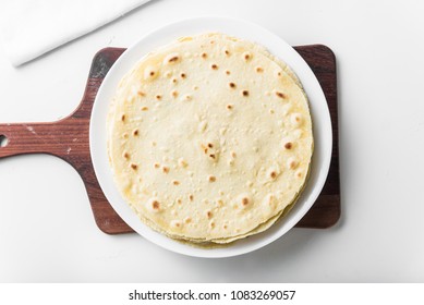Mexican corn tortillas on a white plate on a wooden board. They can be used to make a burrito, takos and quesadilla. Top view