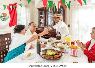 Mexican family enjoying a traditional dinner sitting in a dining room at a home. A young man giving water to his grandmother at a family gathering celebrating the national independence day. - Powered by Shutterstock