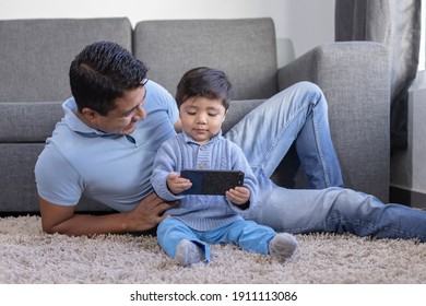 Mexican Father And Son Looking At Phone On Carpet At Home