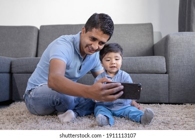 Mexican Father And Son Looking At Phone On Carpet At Home