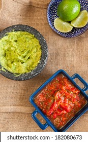 Mexican Fiesta Setting On Table Cloth. Red Salsa, Limes And Guacamole