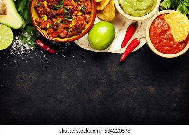 Mexican food concept: tortilla chips, guacamole, salsa, chilli with beans and fresh ingredients over vintage rusty metal background. Top view - Powered by Shutterstock