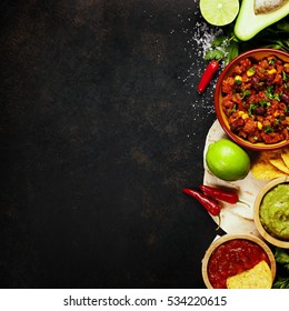 Mexican Food Concept: Tortilla Chips, Guacamole, Salsa, Chilli With Beans And Fresh Ingredients Over Vintage Rusty Metal Background. Top View