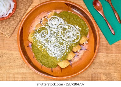 Mexican Food (green Mole Enchiladas) Served With Onion Rings And Aged Cheese In A Clay Dish On A Wooden Table, Decorated With Colorful Napkins Of The Mexican Flag. Top View