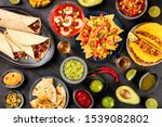 Mexican food, many dishes of the cuisine of Mexico, flat lay, shot from above on a black background. Nachos, tequila, guacamole etc