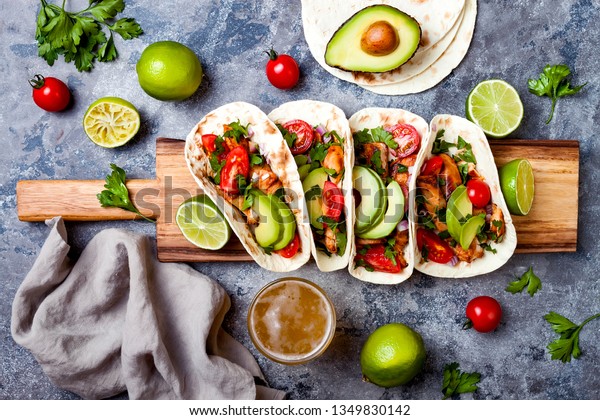 Mexican grilled chicken tacos with avocado, tomato,\
onion on rustic stone table. Recipe for Cinco de Mayo party. Top\
view, overhead, flat lay.\
