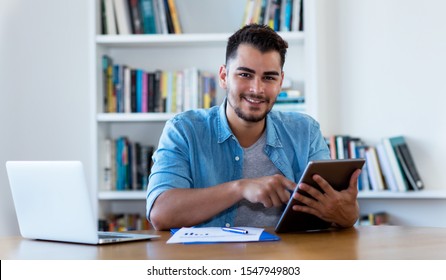 Mexican hipster man reading news with tablet indoor at desk at home 