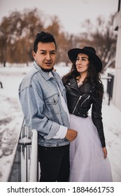 Mexican Hispanic Man In Oversized Denim Jacket And Woman In Hat Leather Biker Jacket Kissing Hugging Laughing Walking.groom Bride Wedding Love Couple In Winter Snow.fashionable Stylish Party Wedding