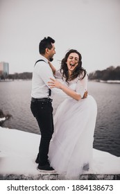 Mexican Hispanic Man In Suspenders And Woman Are Kissing Hugging Laughing. Groom And Bride Wedding Love Couple In Winter In Snow. Fashionable Stylish Party Wedding Wear 2021