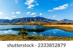 Mexican mountainous panoramic landscape, lake with mirror reflection in water surface, surrounded by arid agricultural land and farms, sunny day along highway Guadalajara to Chapala in Jalisco, Mexico