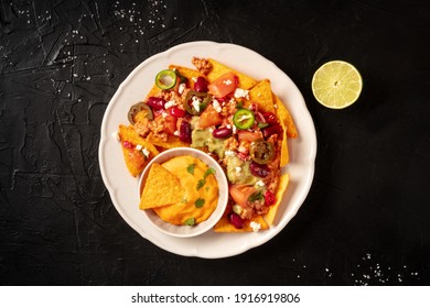 Mexican Nachos With Chili Con Carne, Cheese Dip And A Lime, Overhead Shot On A Black Background