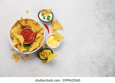 Mexican nachos chips with various sauces - guacamole, salsa, cheese and sour cream. Top view flat lay on stone table with copy space