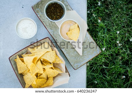 Mexican nachos with three kind sauce served on concrete background in a park. Snack for party, picnic, chips with sauces: cheese and mayonnaise (tartar), copy space. Stock photo © 