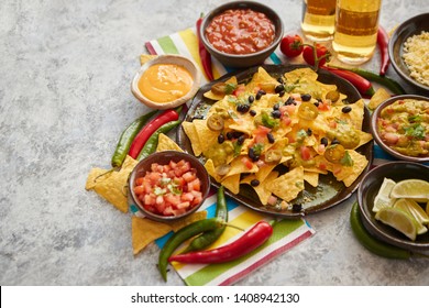 Mexican nachos tortilla chips with black bean, jalapeno, guacamole, tomatoes salsa, cheese and botteled beer. Placed on a table. - Powered by Shutterstock