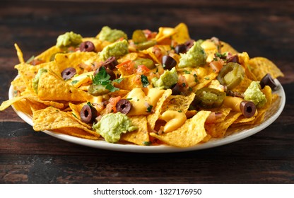 Mexican nachos tortilla chips with olives, jalapeno, guacamole, tomatoes salsa and cheese dip. close up