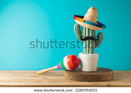 Mexican party concept with cactus, maracas and sombrero hat on wooden table over blue background. Cinco de Mayo holiday celebration