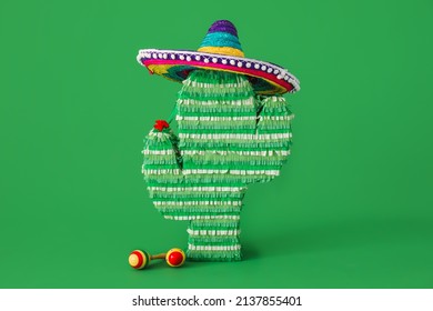 Mexican pinata in shape of cactus with sombrero hat and maracas on green background