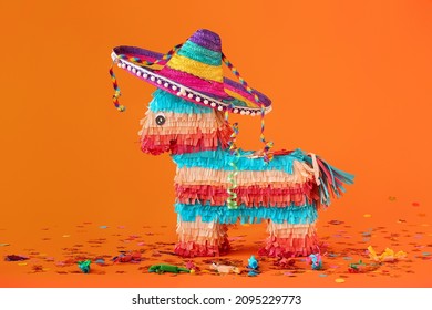 Mexican pinata with sombrero hat and confetti on orange background