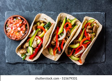 Mexican pork tacos with vegetables and salsa. Tacos al pastor on black stone slate plate on black background. Top view
