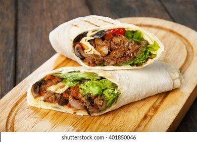 Mexican restaurant fast food - wrapped burritos with pork meat, mushrooms and vegetables closeup at wooden desk on table. Mexican burritos closeup.