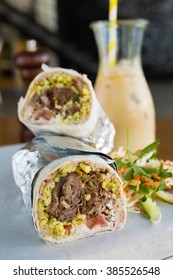 Mexican Shredded Beef Breakfast Burrito Sliced In Half Served With Ice Coffee.