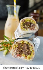 Mexican Shredded Beef Breakfast Burrito Sliced In Half Served With Ice Coffee.