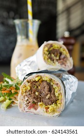 Mexican Shredded Beef Breakfast Burrito Sliced In Half Served With Ice Coffee.