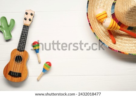 Mexican sombrero hat, maracas, toy cactus and guitar on white wooden background, flat lay. Space for text