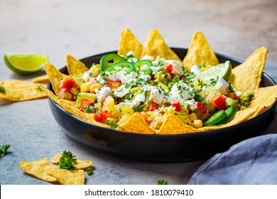 Mexican street corn salad with cheese and nachos chips in a black platter. Mexican food concept.