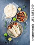 Mexican style burritos - tortilla wrap with spicy chicken meat breast filet nuggets, vegetables and black olives served as top view with hot spices on a design plate 